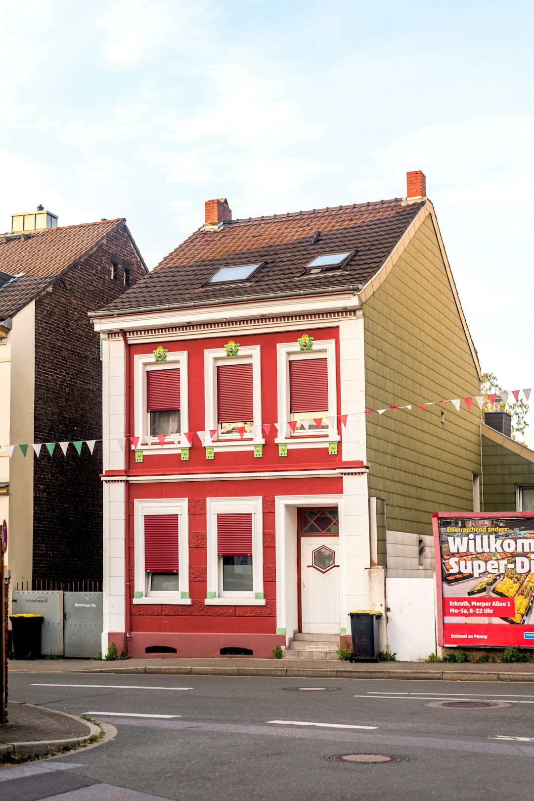 A narrow red house with white trim and green shutters